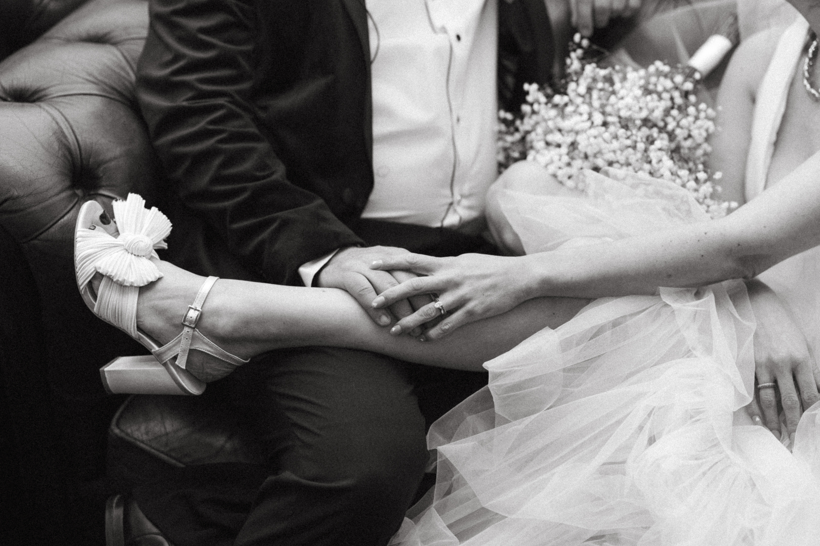 Black and white photo of a groom and bride sitting together. Women's leg across the mans lap.
