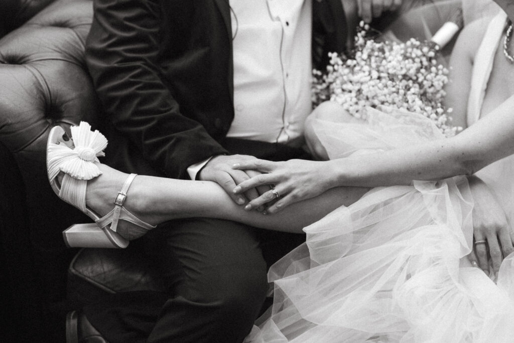 Black and white image of a bride and groom sitting together. Woman's legs are across the man's lap.